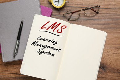 Image of Notebook with text Learning Management System and its abbreviation LMS on wooden table, flat lay
