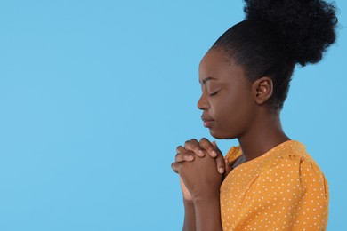 Photo of Woman with clasped hands praying to God on light blue background. Space for text