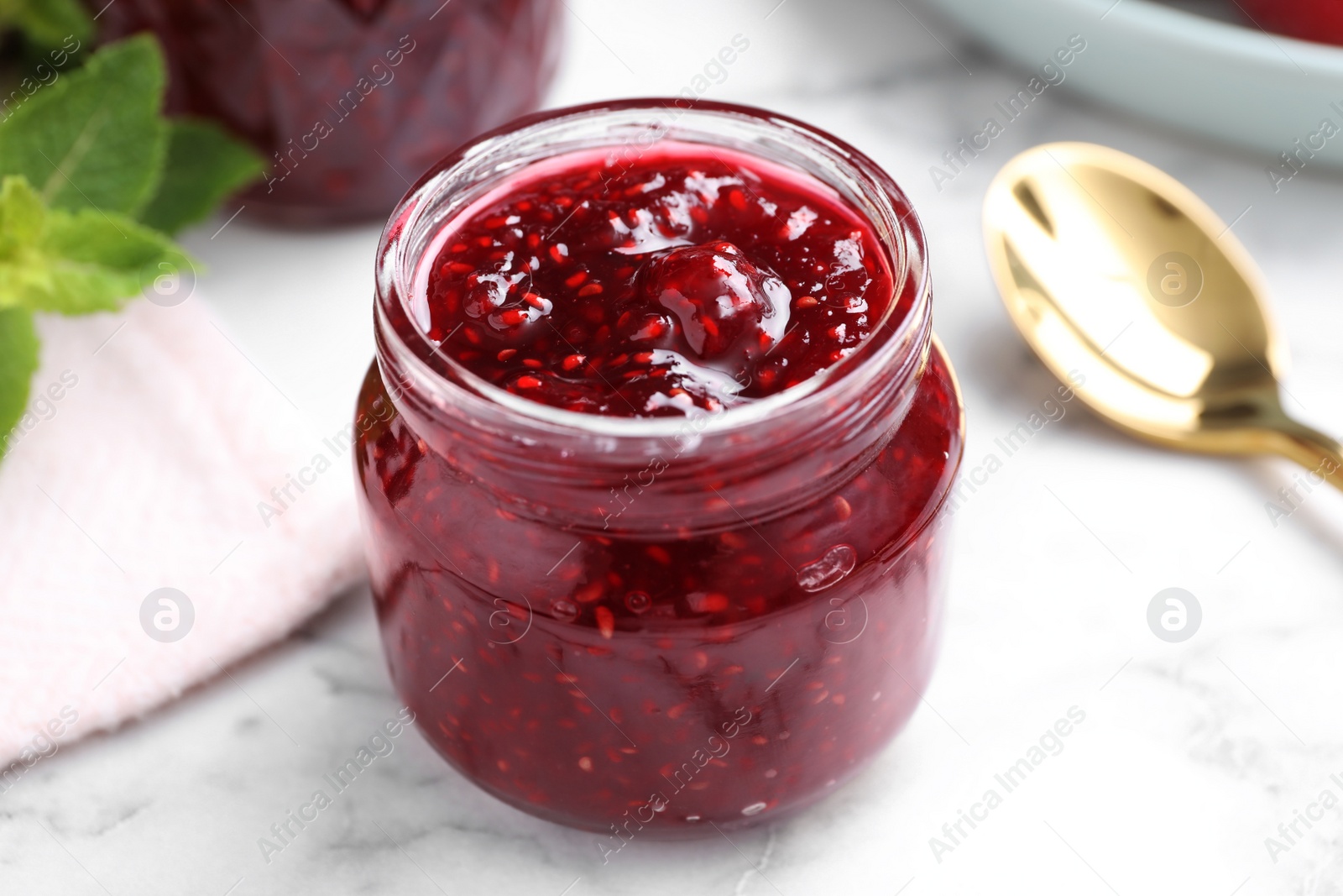 Photo of Delicious raspberry jam on white marble table, closeup