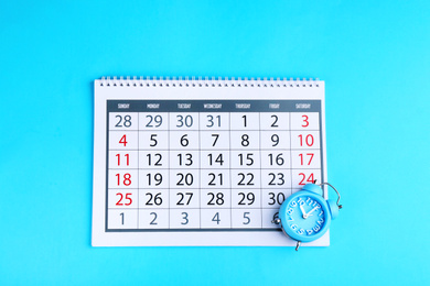 Photo of Calendar and alarm clock on light blue background, flat lay