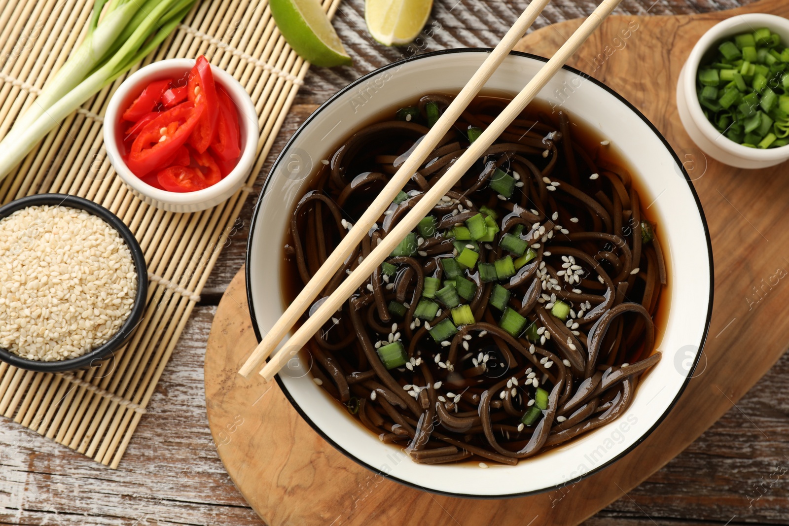 Photo of Tasty soup with buckwheat noodles (soba) and onion in bowl served on wooden table, flat lay