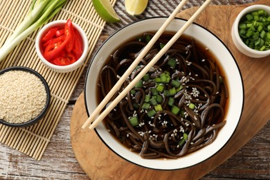 Photo of Tasty soup with buckwheat noodles (soba) and onion in bowl served on wooden table, flat lay