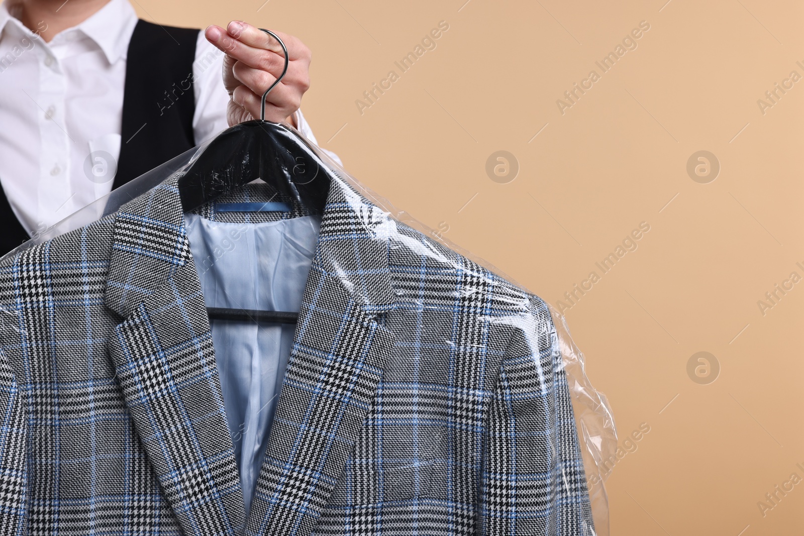 Photo of Dry-cleaning service. Woman holding jacket in plastic bag on beige background, closeup. Space for text