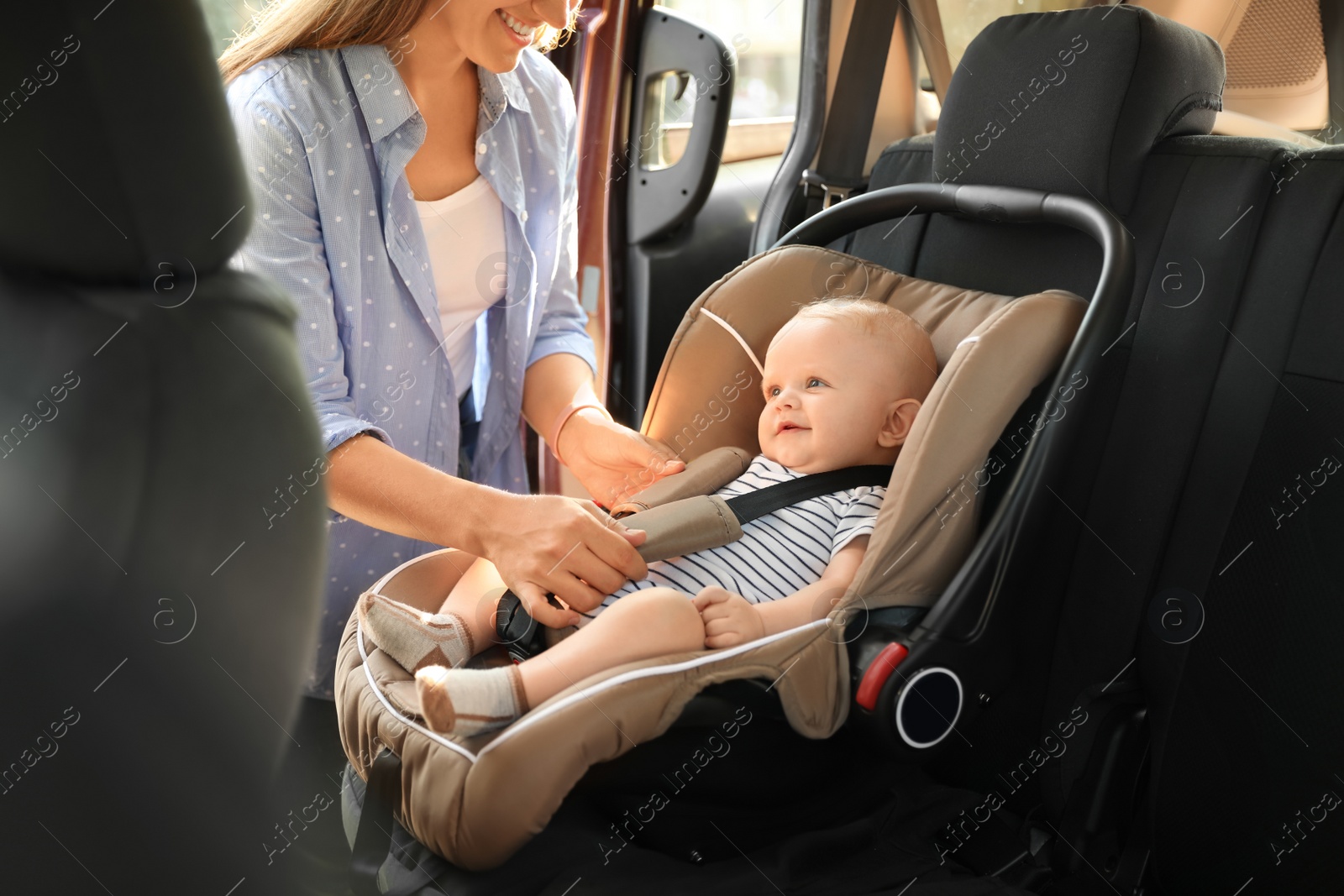 Photo of Mother fastening baby to child safety seat inside of car