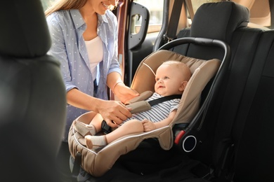 Photo of Mother fastening baby to child safety seat inside of car