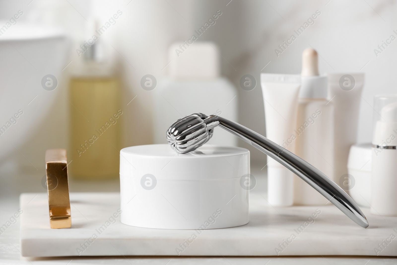 Photo of Tray with metal face roller and cosmetic products on counter in bathroom, closeup