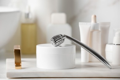 Photo of Tray with metal face roller and cosmetic products on counter in bathroom, closeup