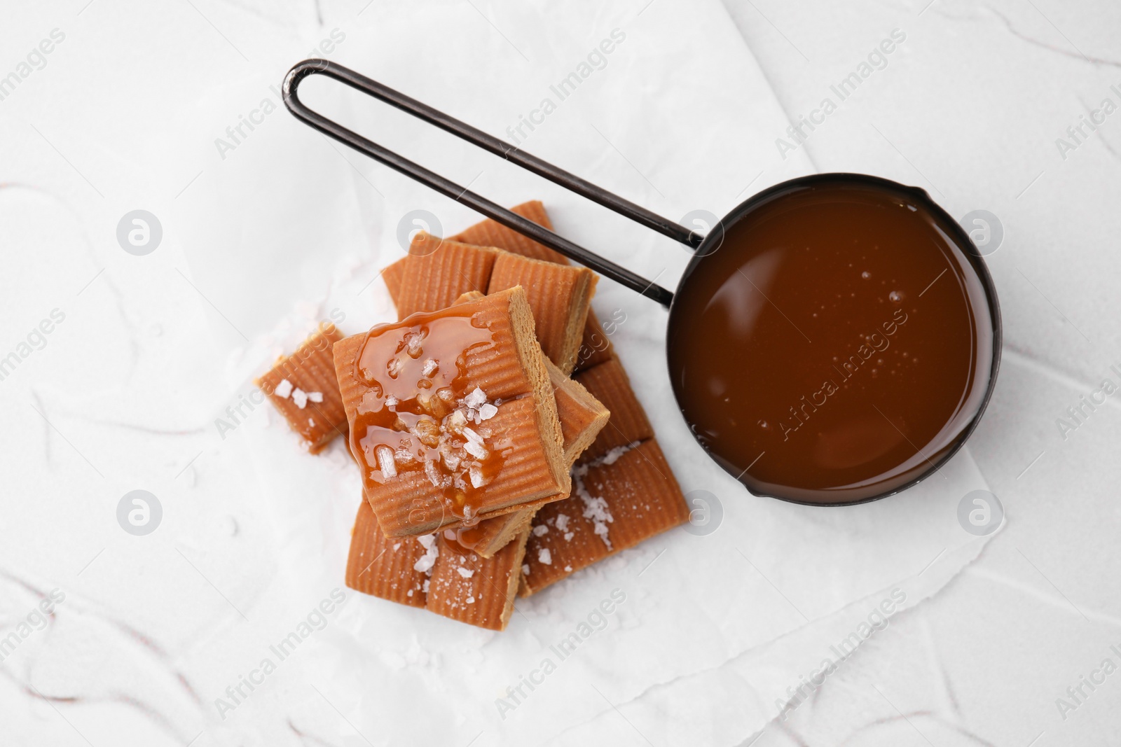 Photo of Yummy caramel candies, sauce and sea salt on white table, top view