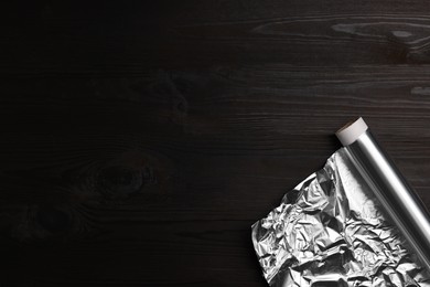 Roll of aluminum foil on dark wooden table, top view. Space for text