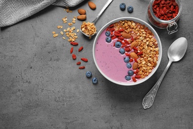 Photo of Flat lay composition of smoothie bowl with goji berries on grey table. Space for text