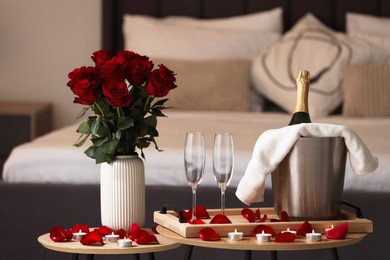 Honeymoon. Sparkling wine, glasses and bouquet of roses on wooden table in room