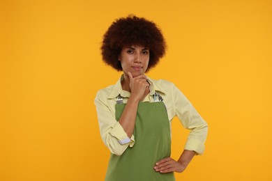 Photo of Thoughtful young woman in apron on orange background