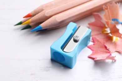 Photo of Colorful pencils, sharpener and shavings on white wooden background, closeup