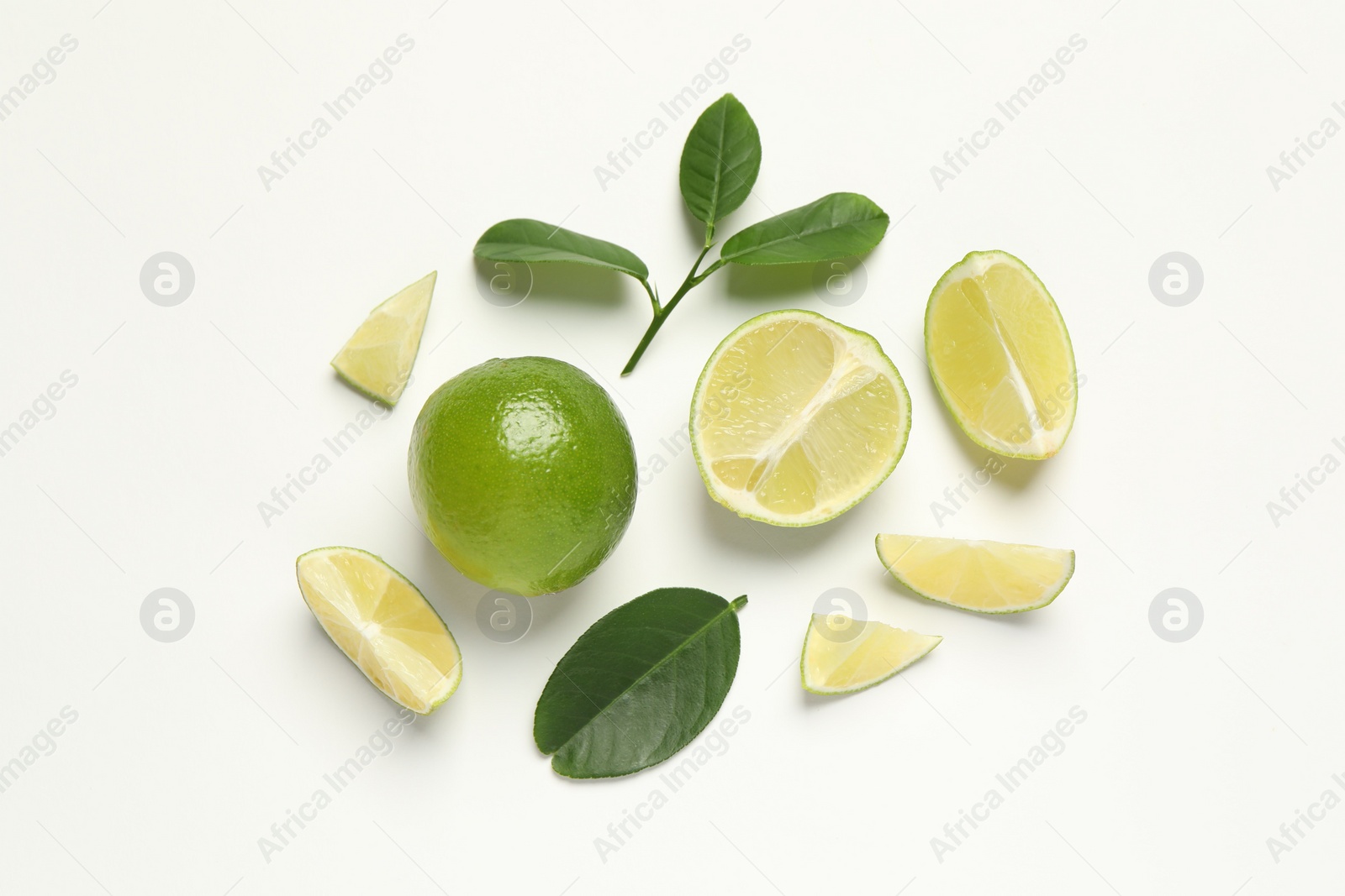 Photo of Whole and cut fresh ripe limes with green leaves on white background, flat lay