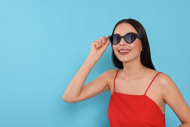 Photo of Attractive happy woman touching fashionable sunglasses against light blue background. Space for text