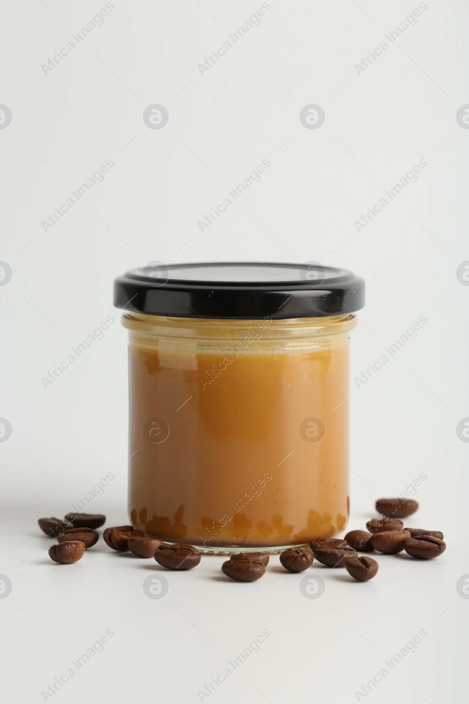 Photo of Tasty salted caramel in jar and coffee beans on white background, space for text