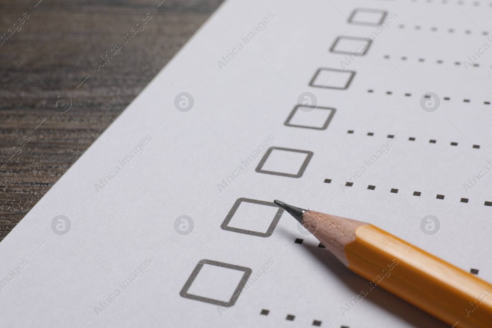 Photo of Paper sheet with checkboxes and pencil on wooden table, closeup. Checklist