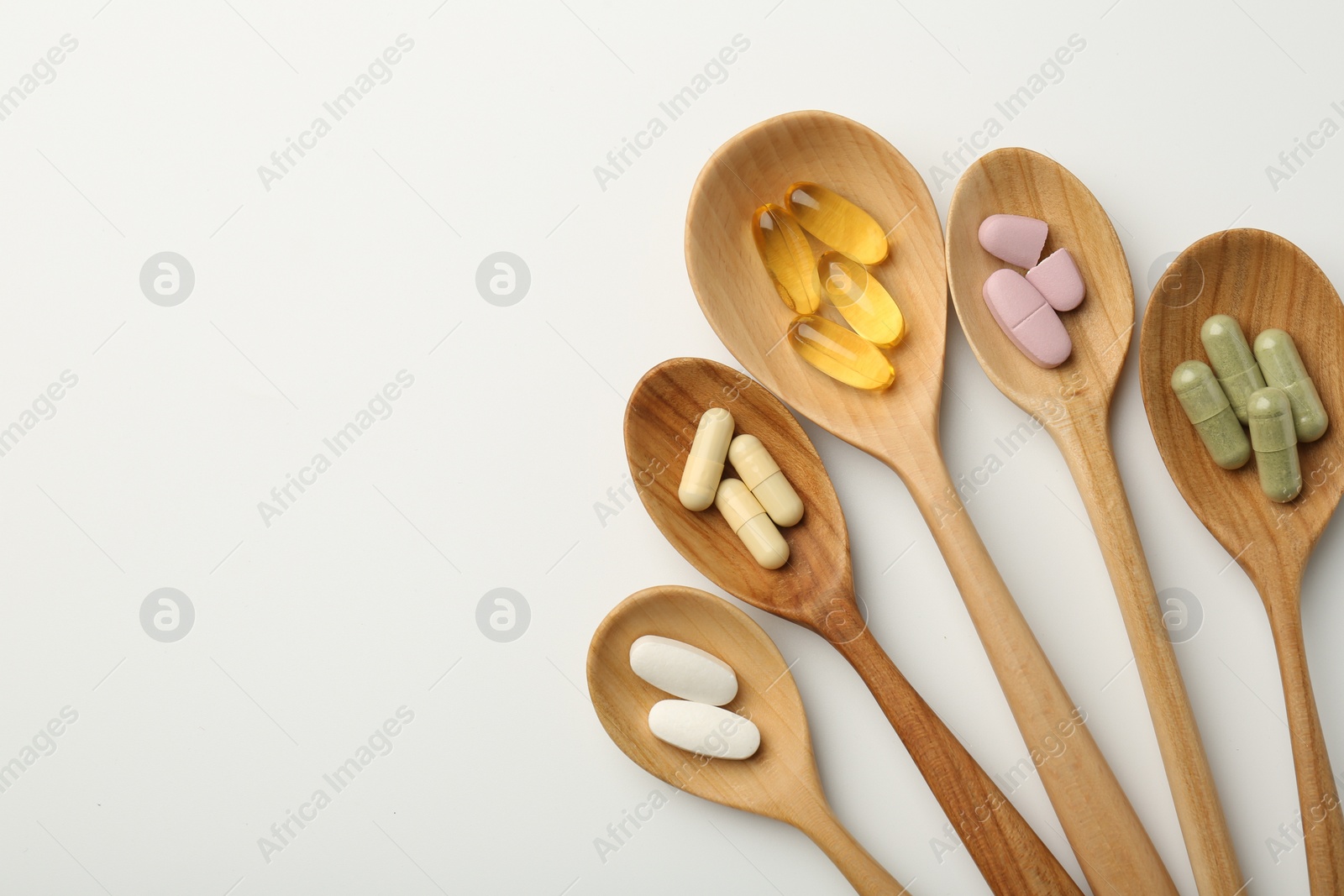 Photo of Vitamin capsules in wooden spoons on white background, flat lay. Space for text