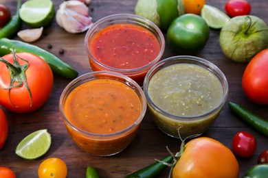 Photo of Tasty salsa sauces and ingredients on wooden table