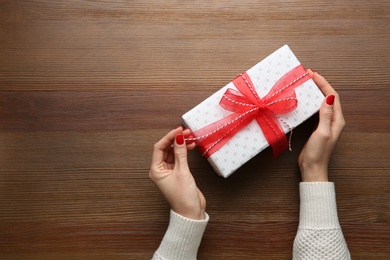 Photo of Woman holding white Christmas gift box at wooden table, top view. Space for text