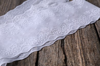 Photo of White lace with beautiful pattern on wooden table, closeup