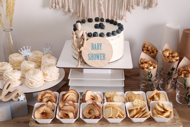 Photo of Baby shower party. Different delicious treats and decor on wooden table near light wall