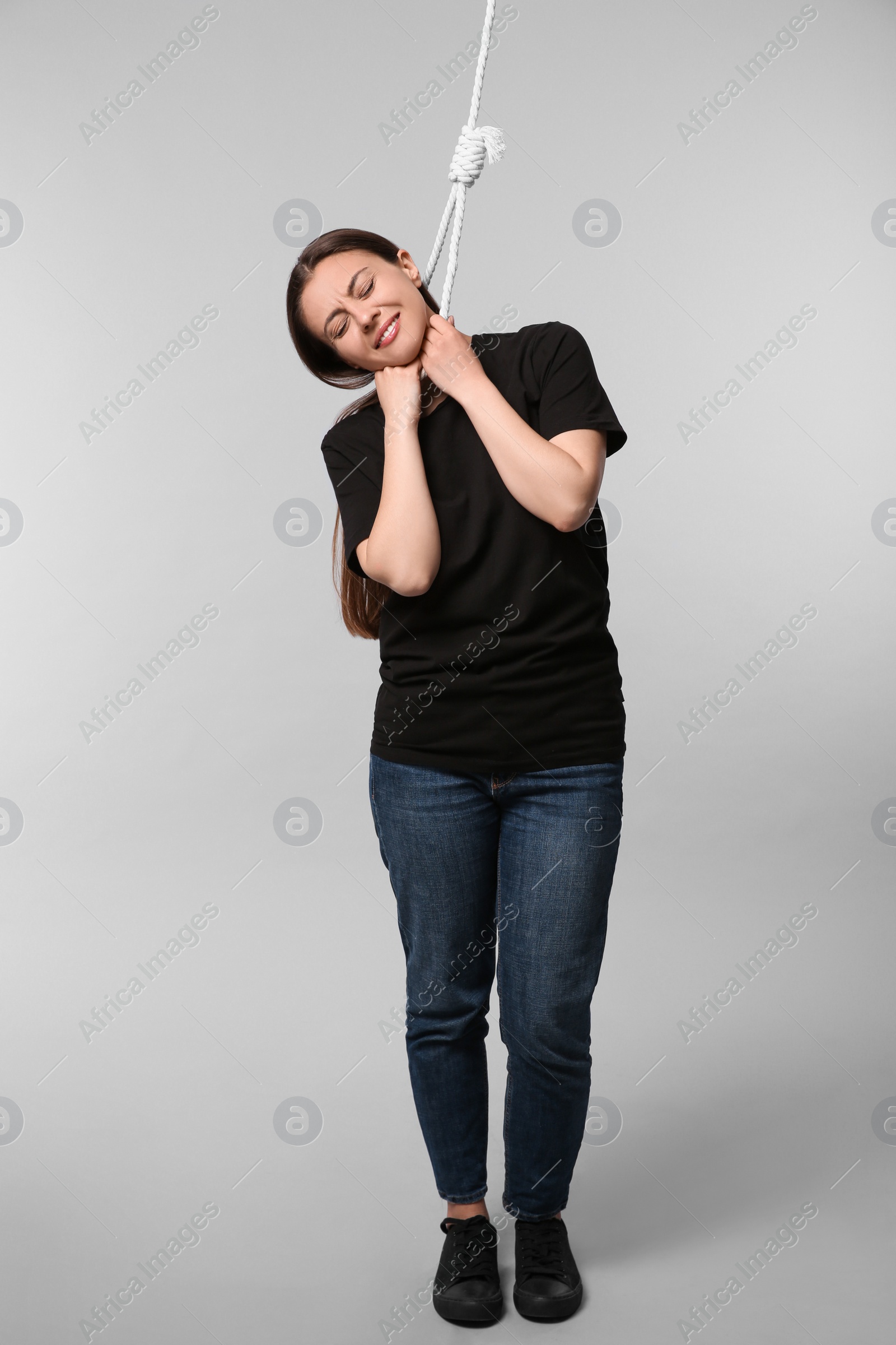 Photo of Depressed woman with rope noose on neck against light grey background