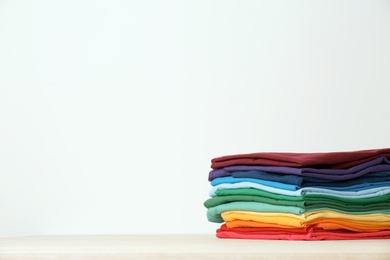 Photo of Stack of bright folded clothes on table against white background. Space for text