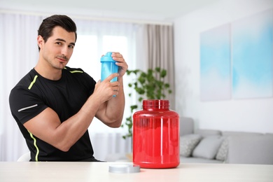 Young athletic man with protein shake at home, space for text