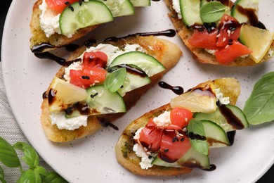Delicious bruschettas with balsamic vinegar and toppings on plate, flat lay