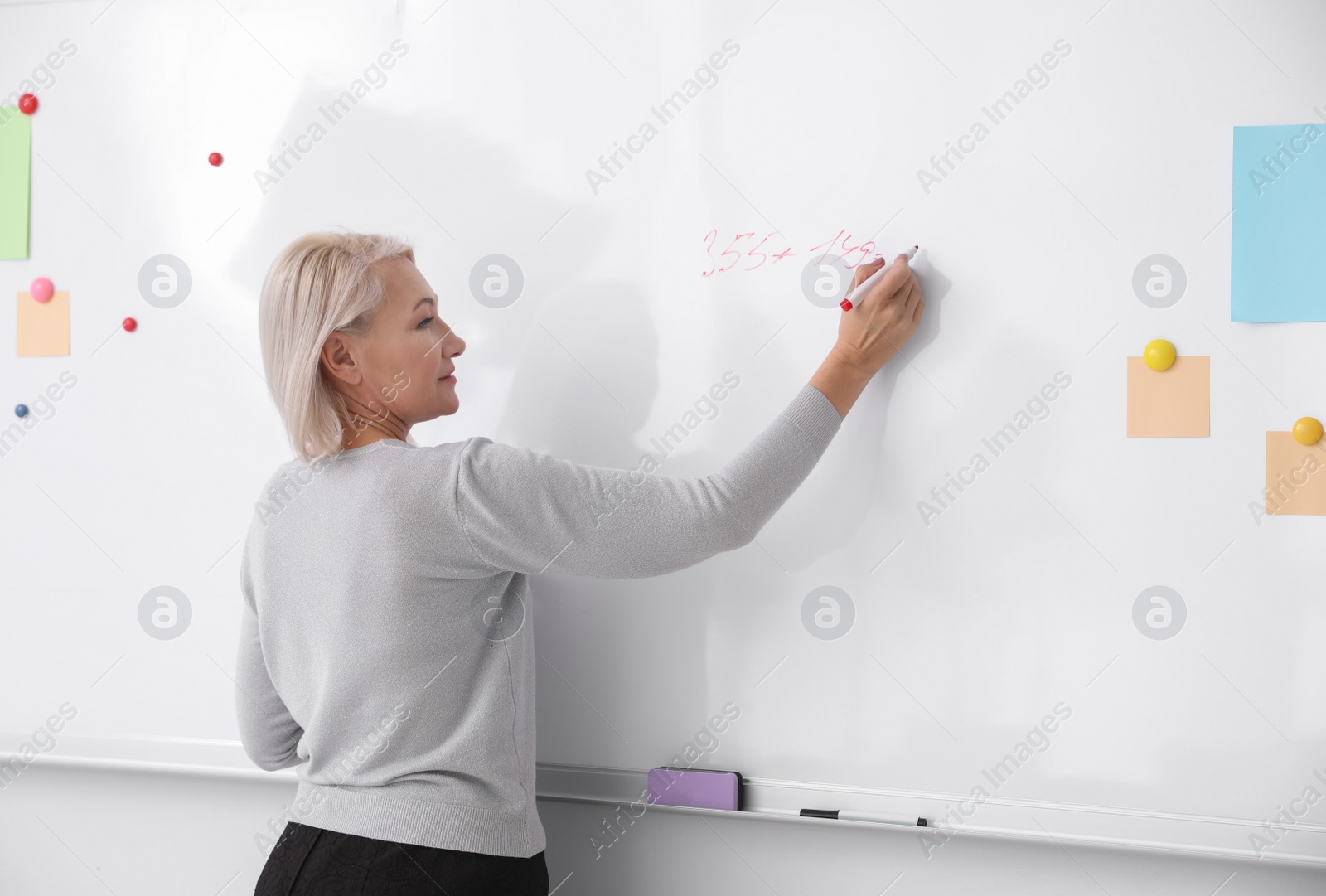 Photo of Mature teacher writing on whiteboard in classroom