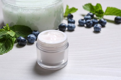Jar of body cream and blueberry on light wooden background