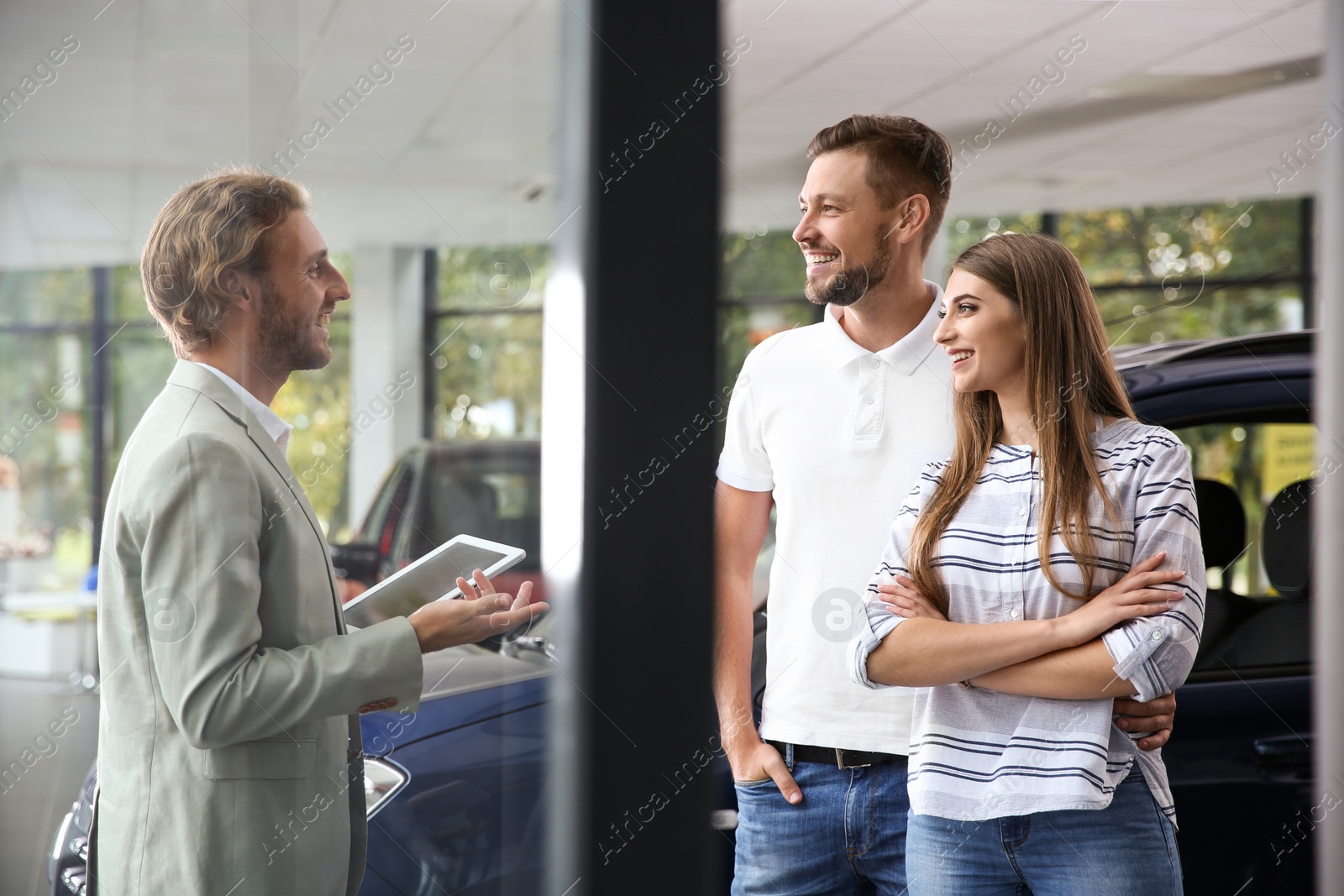 Photo of Salesman with tablet consulting young couple in car dealership
