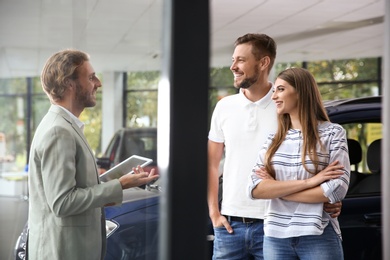 Salesman with tablet consulting young couple in car dealership