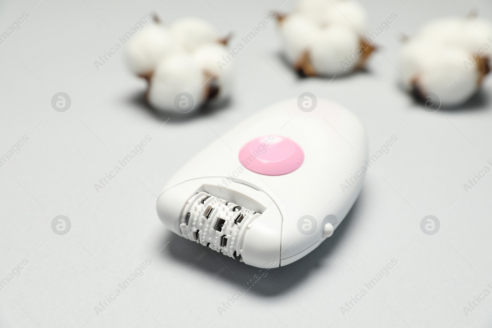 Photo of Modern epilator and fluffy cotton flowers on white background, closeup