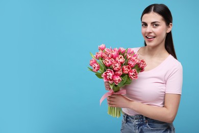 Photo of Happy young woman with beautiful bouquet on light blue background. Space for text