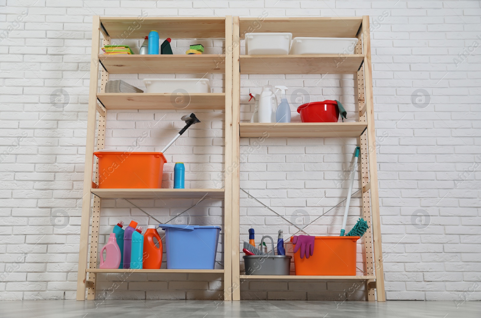 Photo of Wooden shelving units with cleaning equipment near white brick wall. Stylish room interior