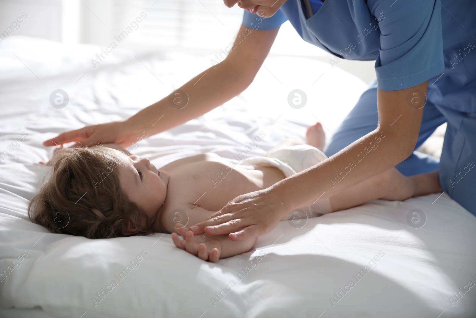 Photo of Orthopedist examining cute little baby on bed