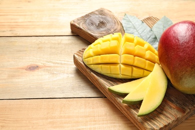 Photo of Board with fresh mango on wooden table. Space for text