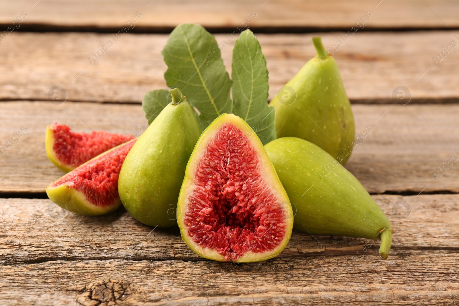 Photo of Cut and whole green figs on wooden table, closeup