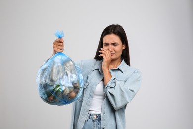 Photo of Woman holding full garbage bag on light background