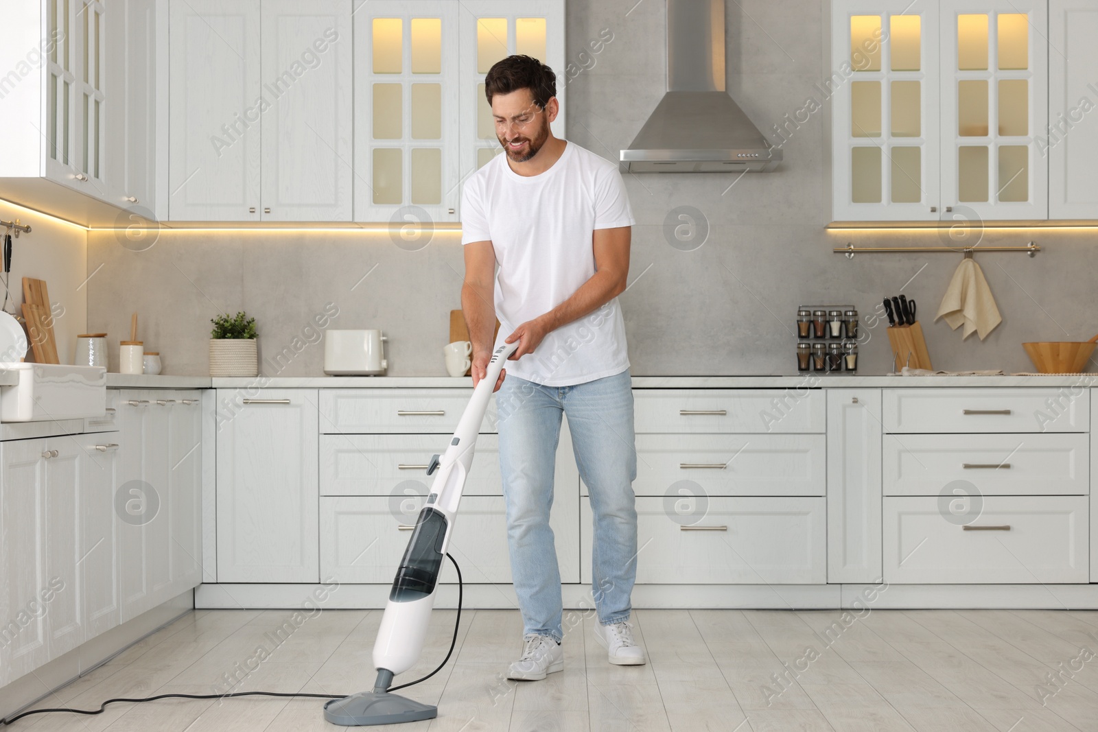 Photo of Happy man cleaning floor with steam mop in kitchen at home