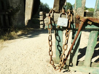 Old wooden fence with metal chain and lock on sunny day, space for text