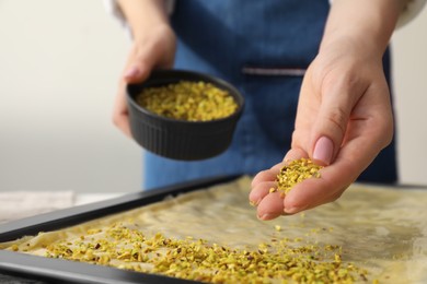 Photo of Making delicious baklava. Woman adding chopped nuts to dough at white table, closeup