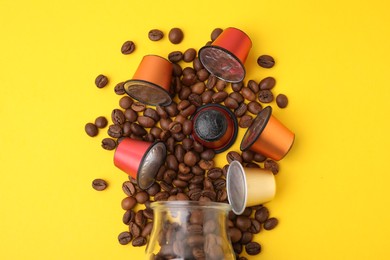Photo of Many coffee capsules, beans and glass jar on yellow background, flat lay