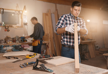 Photo of Professional carpenter and colleague working with wooden plank in workshop