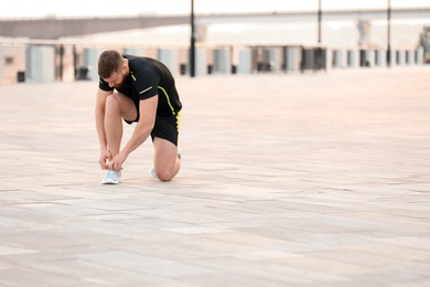 Young man tying shoelaces before running outdoors on sunny day