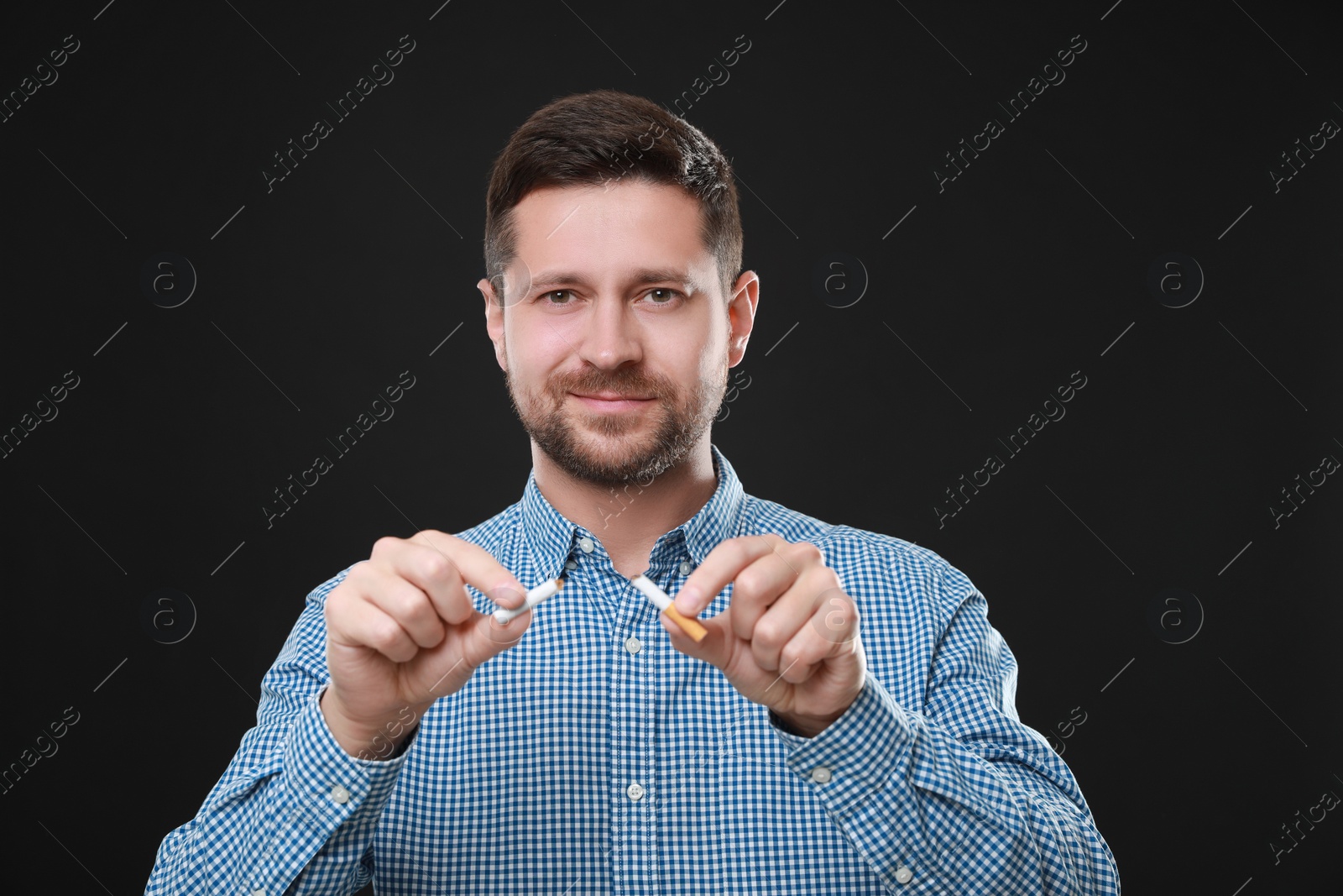 Photo of Stop smoking concept. Man holding pieces of broken cigarette on black background