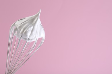Photo of Whisk with whipped cream on pink background. Space for text