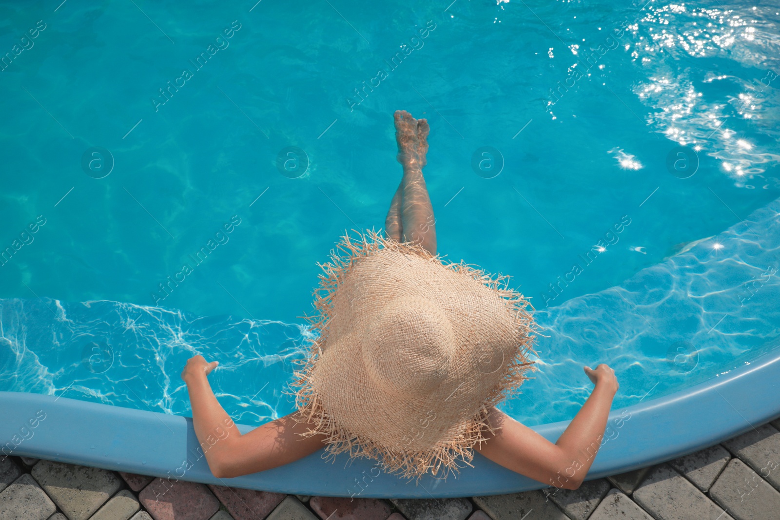 Photo of African American woman with straw hat resting in outdoor swimming pool on sunny summer day, top view